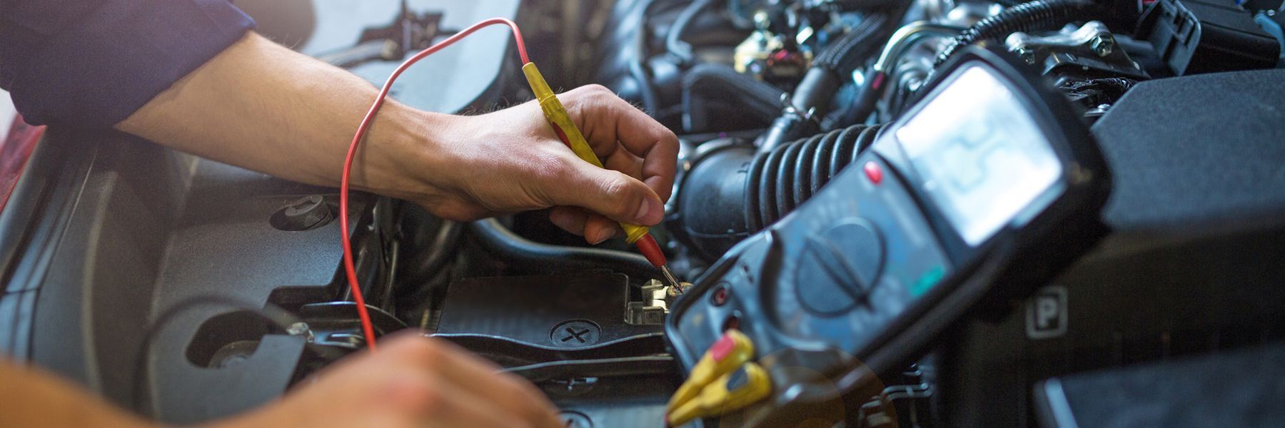 A person is working on a car with a multimeter.