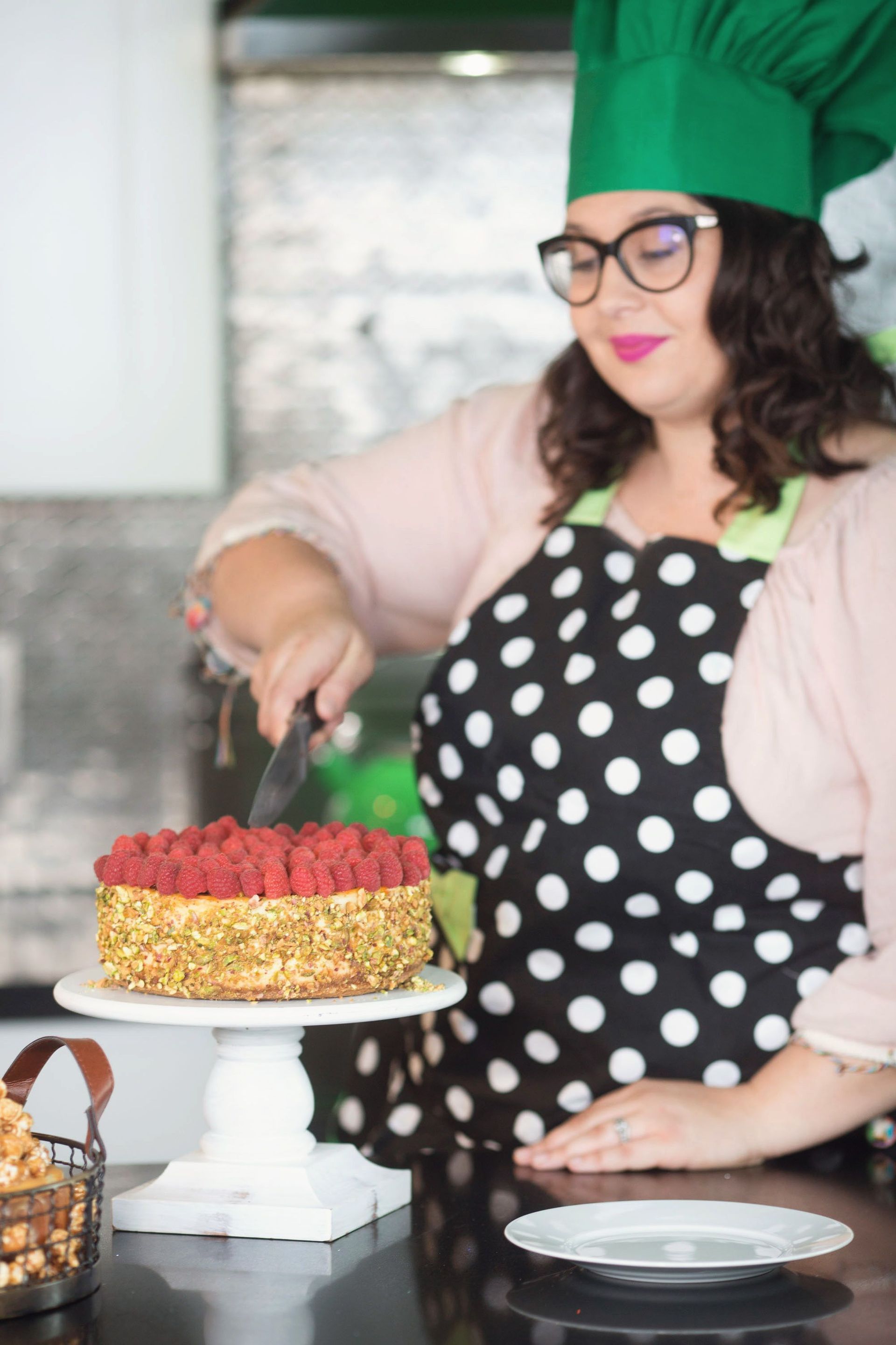A woman in a chef 's hat is cutting a cake in a kitchen.