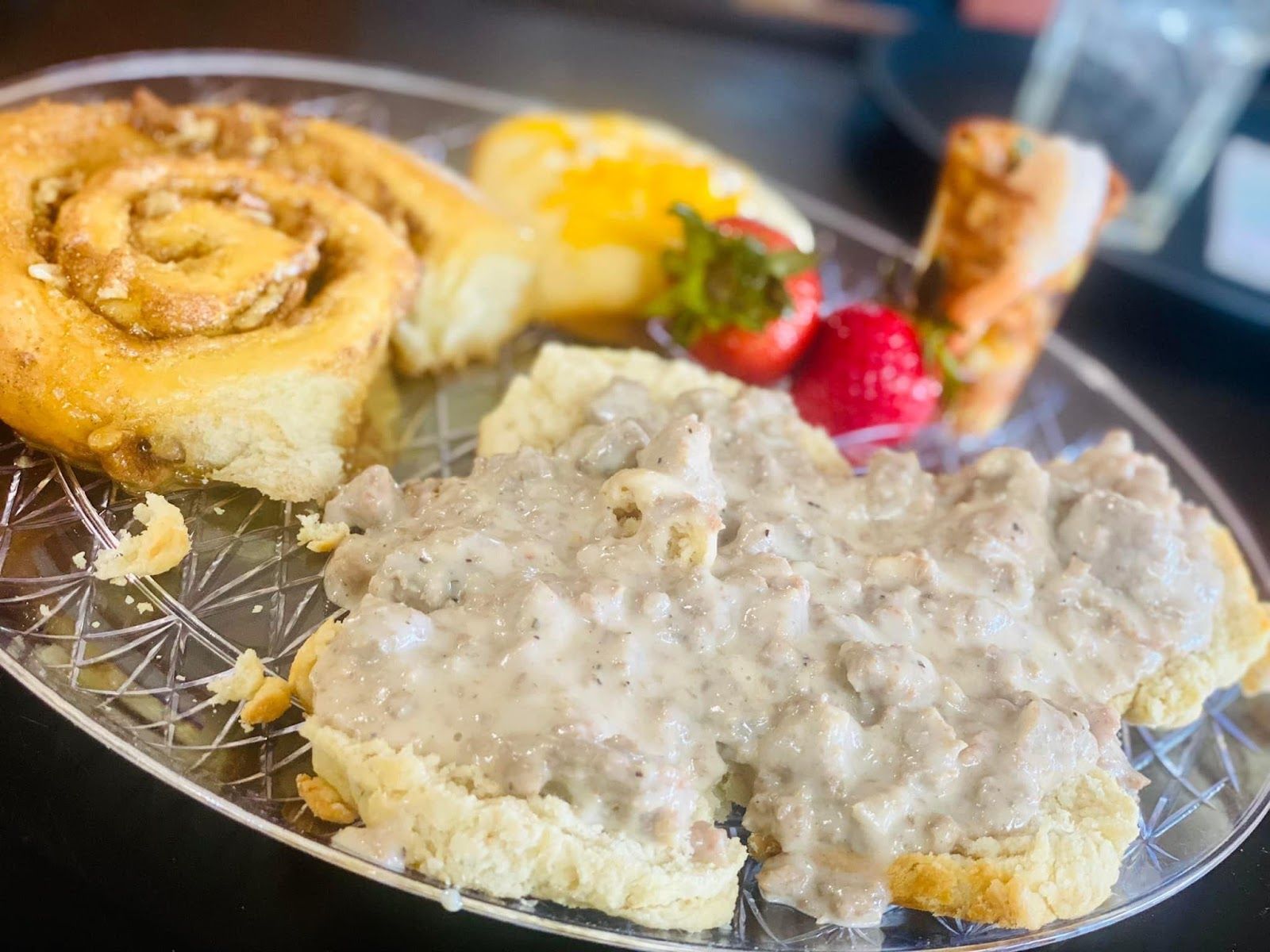 A plate of food with gravy , biscuits , cinnamon rolls and strawberries on a table.