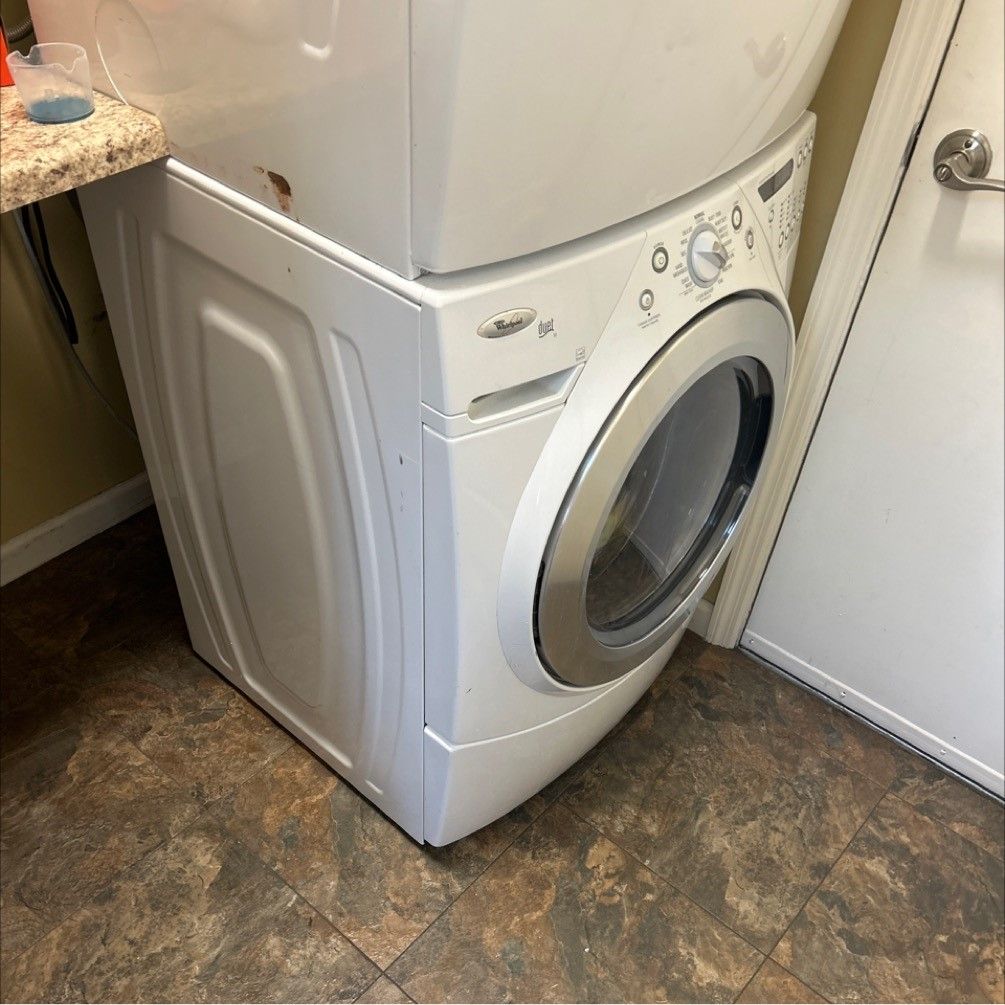 A stacked white Whirlpool washer and dryer in a laundry room, next to a door and countertop.