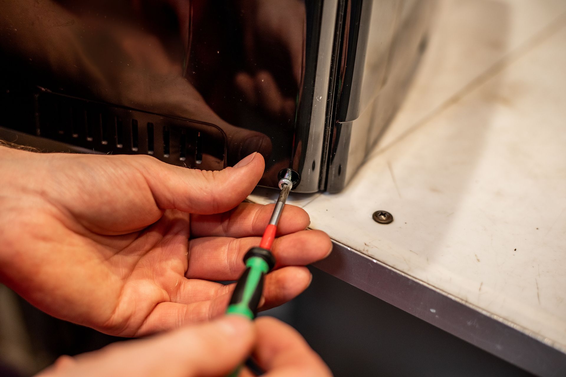 Hands of a repairman carefully unfasten screws securing the rear panel of the coffee machine.