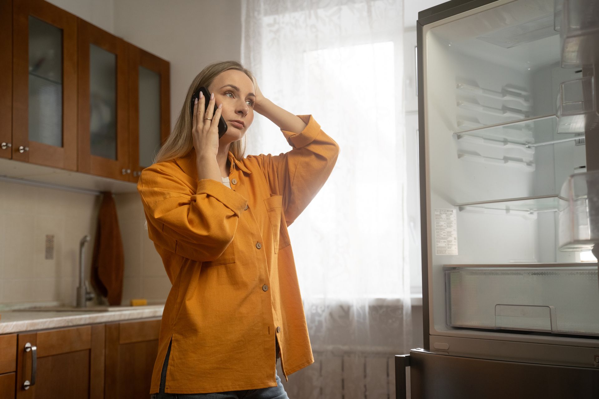 Blond woman with yellow shirt in front of open refrigerator calling a repairman. Blond woman with yellow shirt in front of open refrigerator calling a repairman.