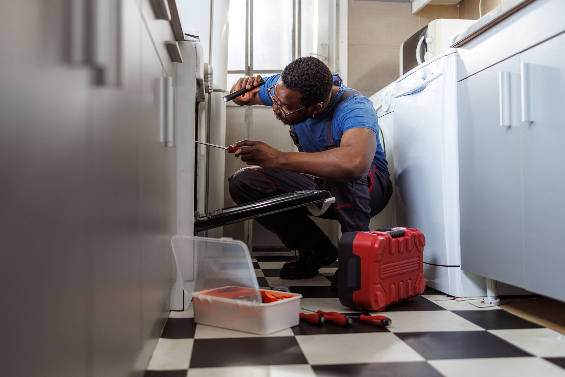 A handyman repairing a stove in a client's kitchen.