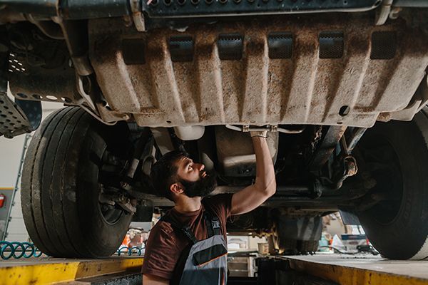 Mechanic inspects underside of a vehicle raised on a lift in a garage.