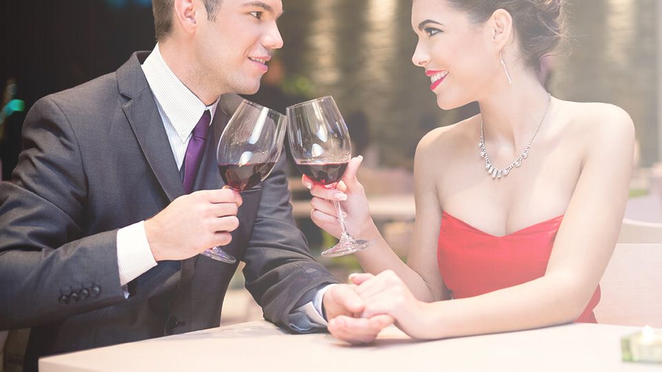 A man and a woman are sitting at a table holding hands and drinking wine.