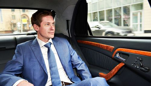 A man in a suit and tie is sitting in the back seat of a car.