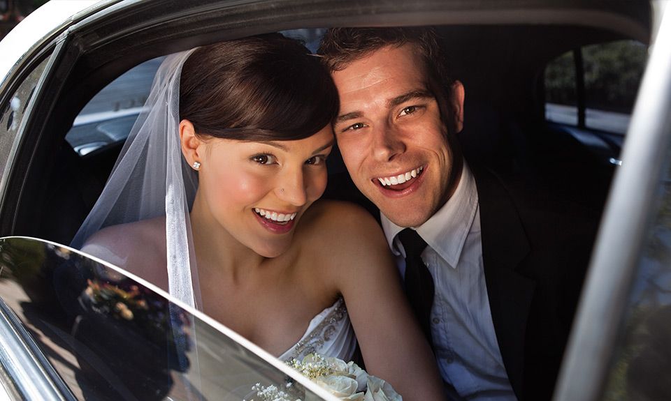 A bride and groom are sitting in the back seat of a car.