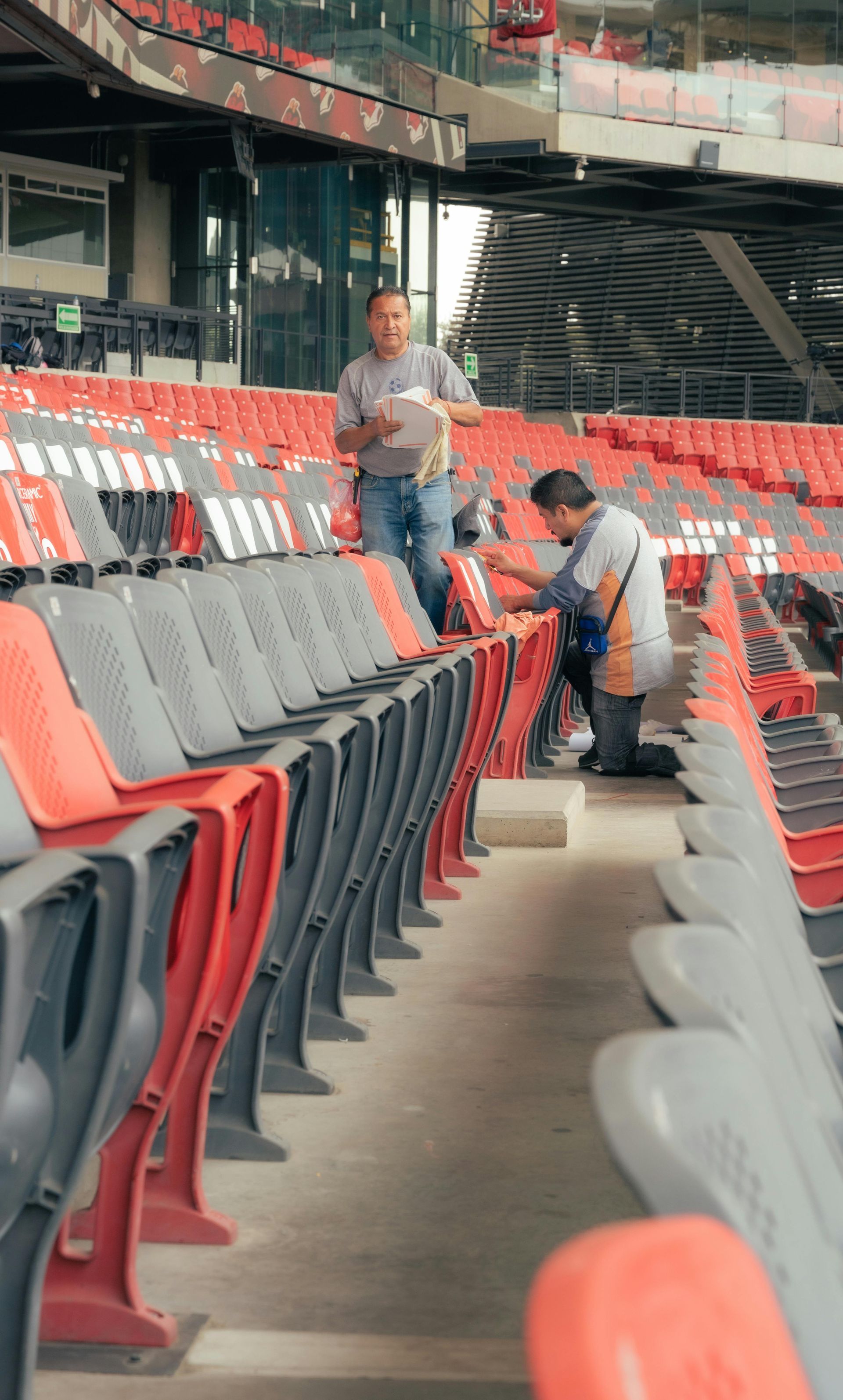 Two men are working on the seats in a stadium.