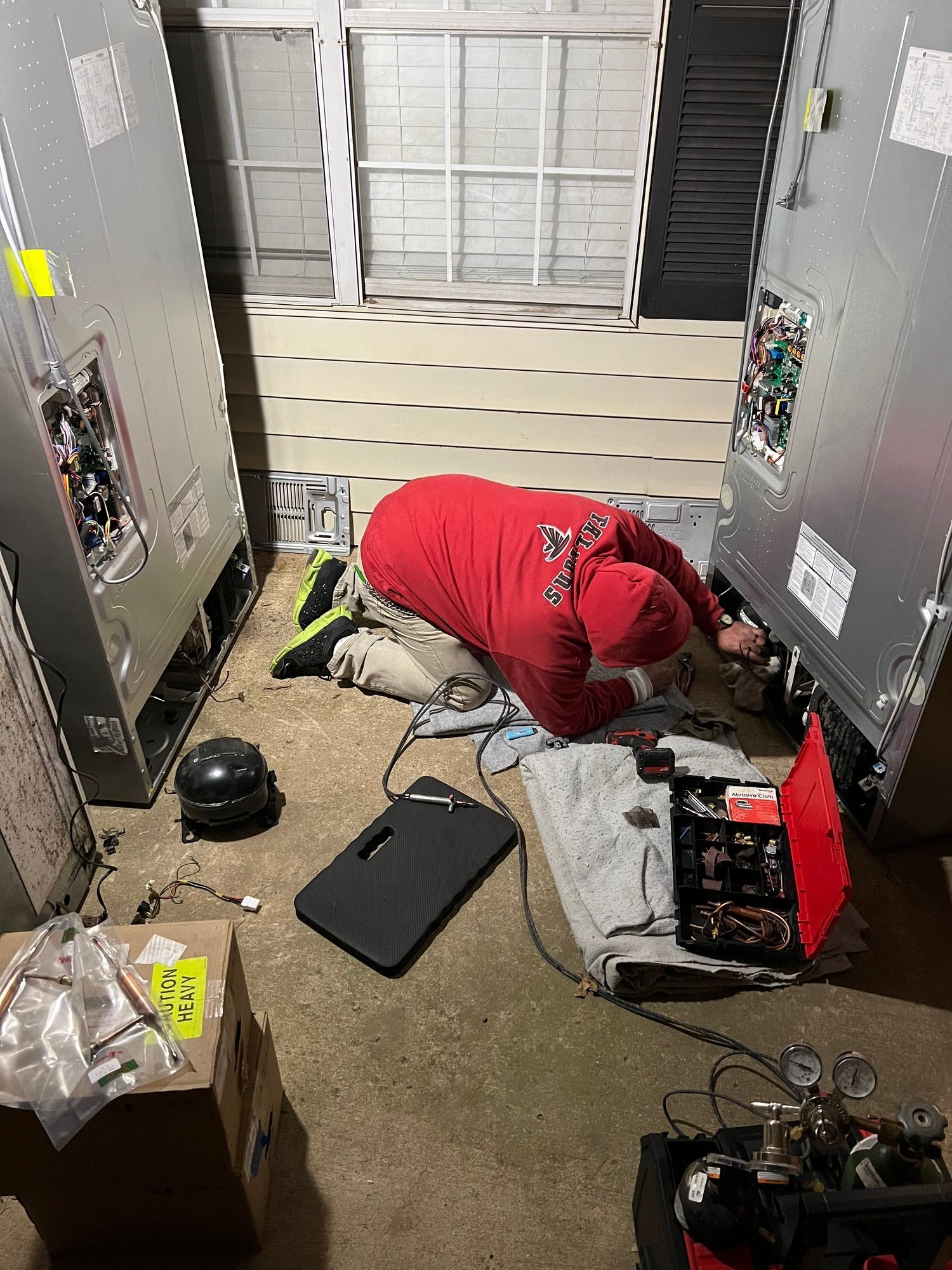 A man is working on a refrigerator in a garage.