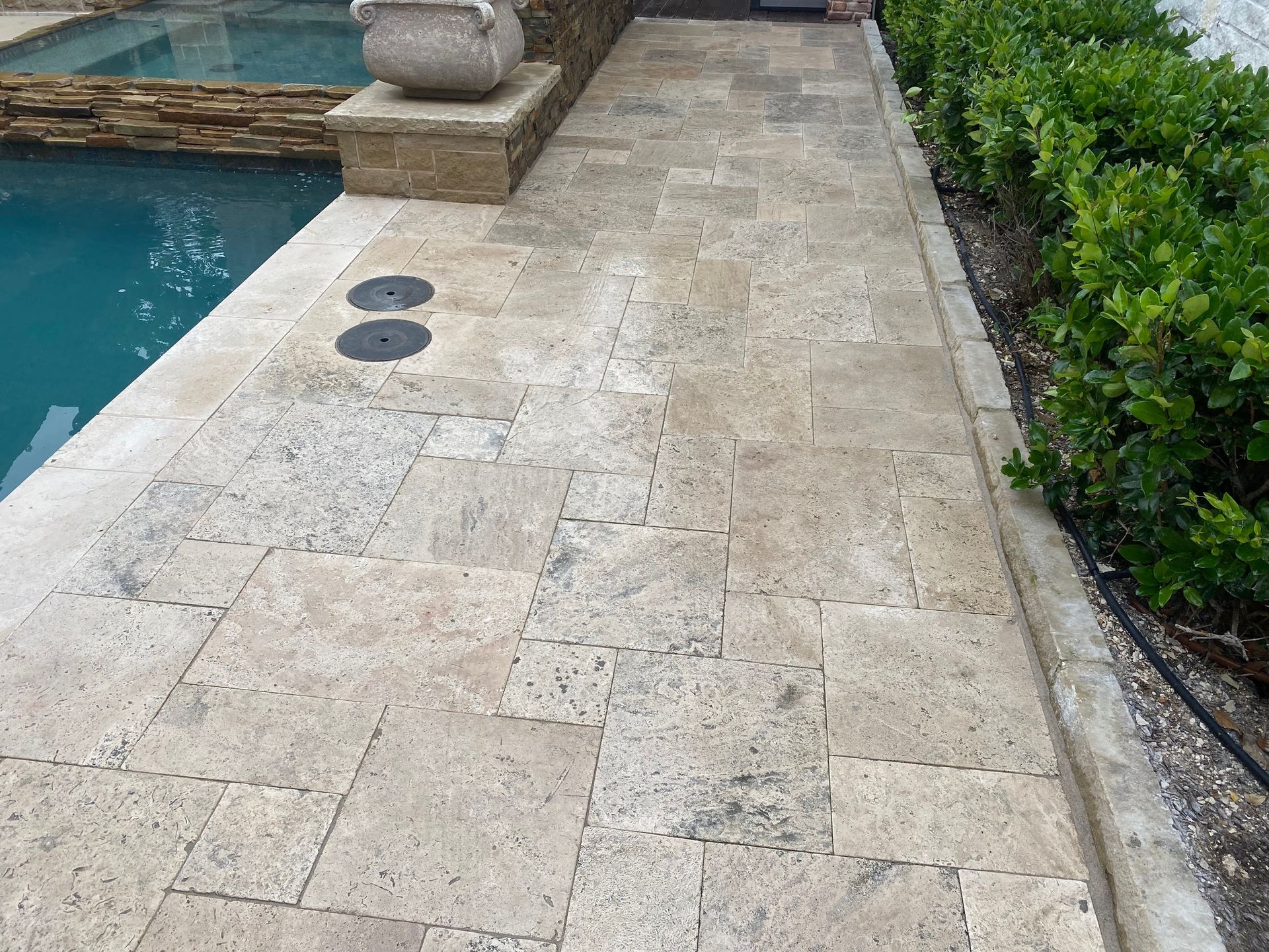 A walkway next to a swimming pool with a planter on top of it.