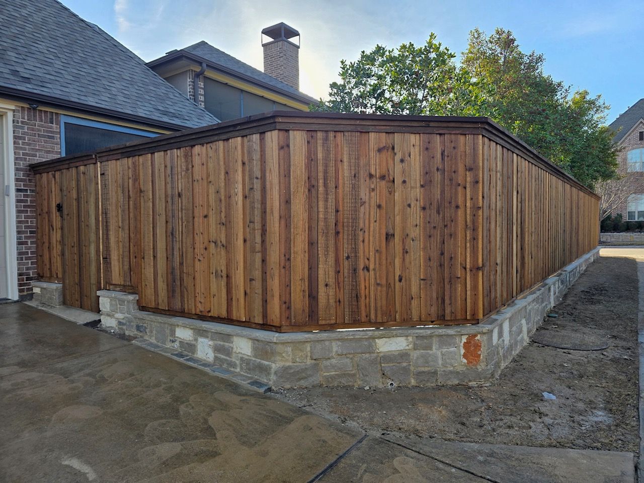 A wooden fence is surrounding a stone wall in front of a house.