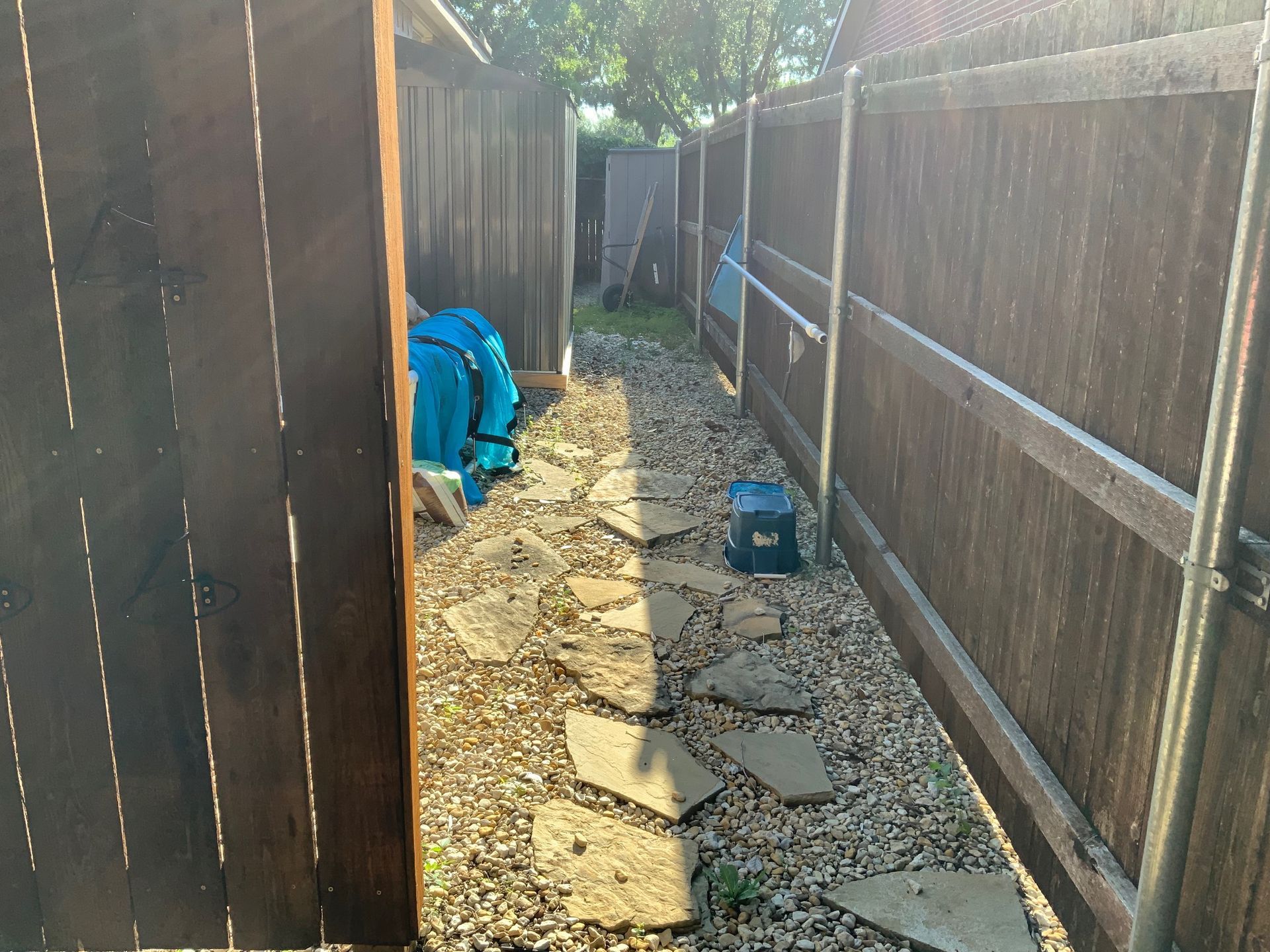 A wooden fence surrounds a gravel path in a backyard.