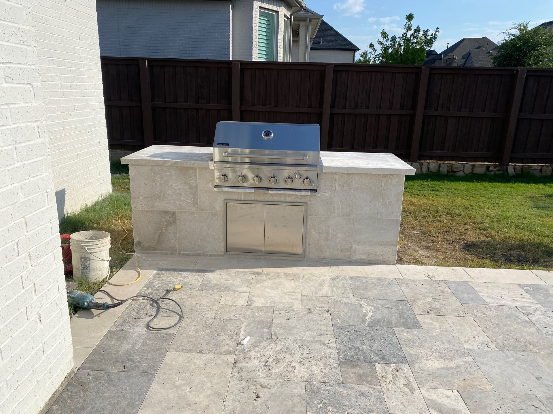 A patio with a grill and a fence in the background