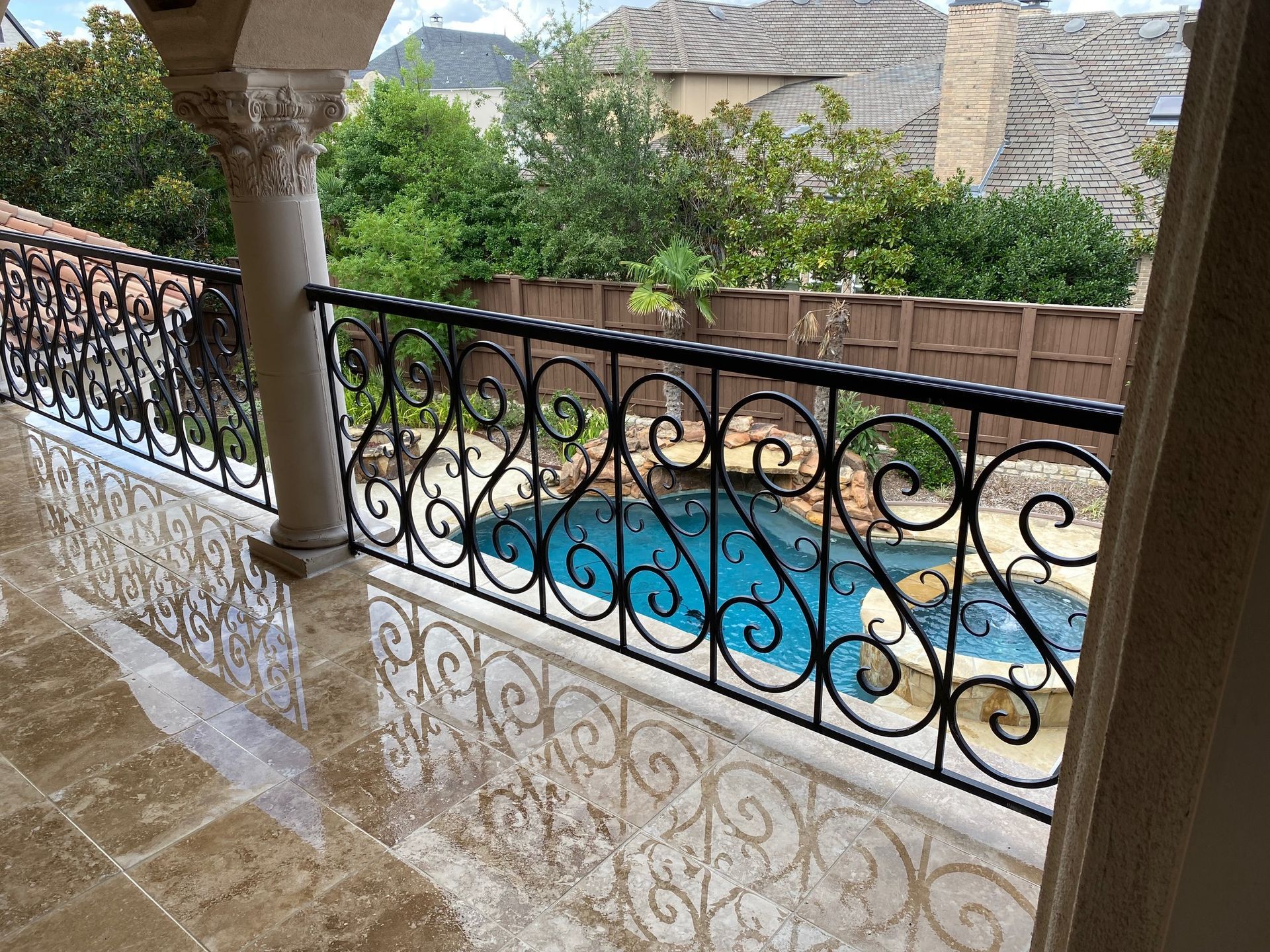 A balcony with a wrought iron railing overlooking a swimming pool.
