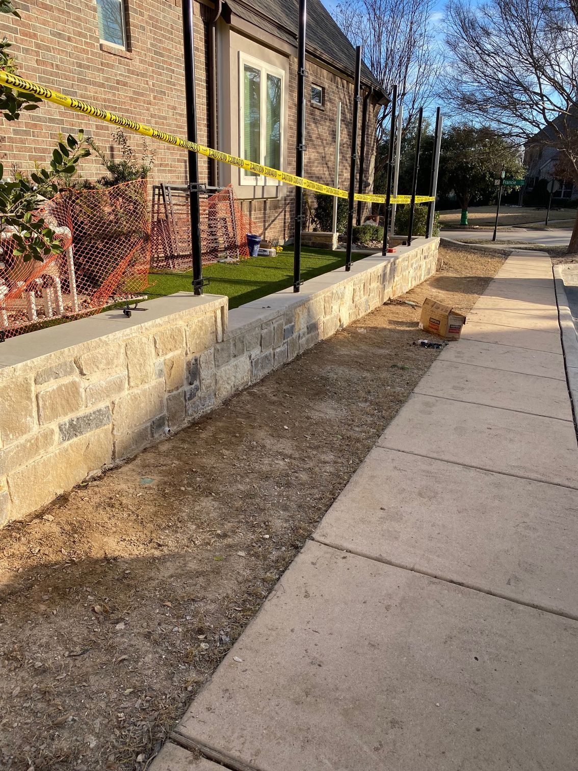 A brick wall is being built next to a sidewalk in front of a house.