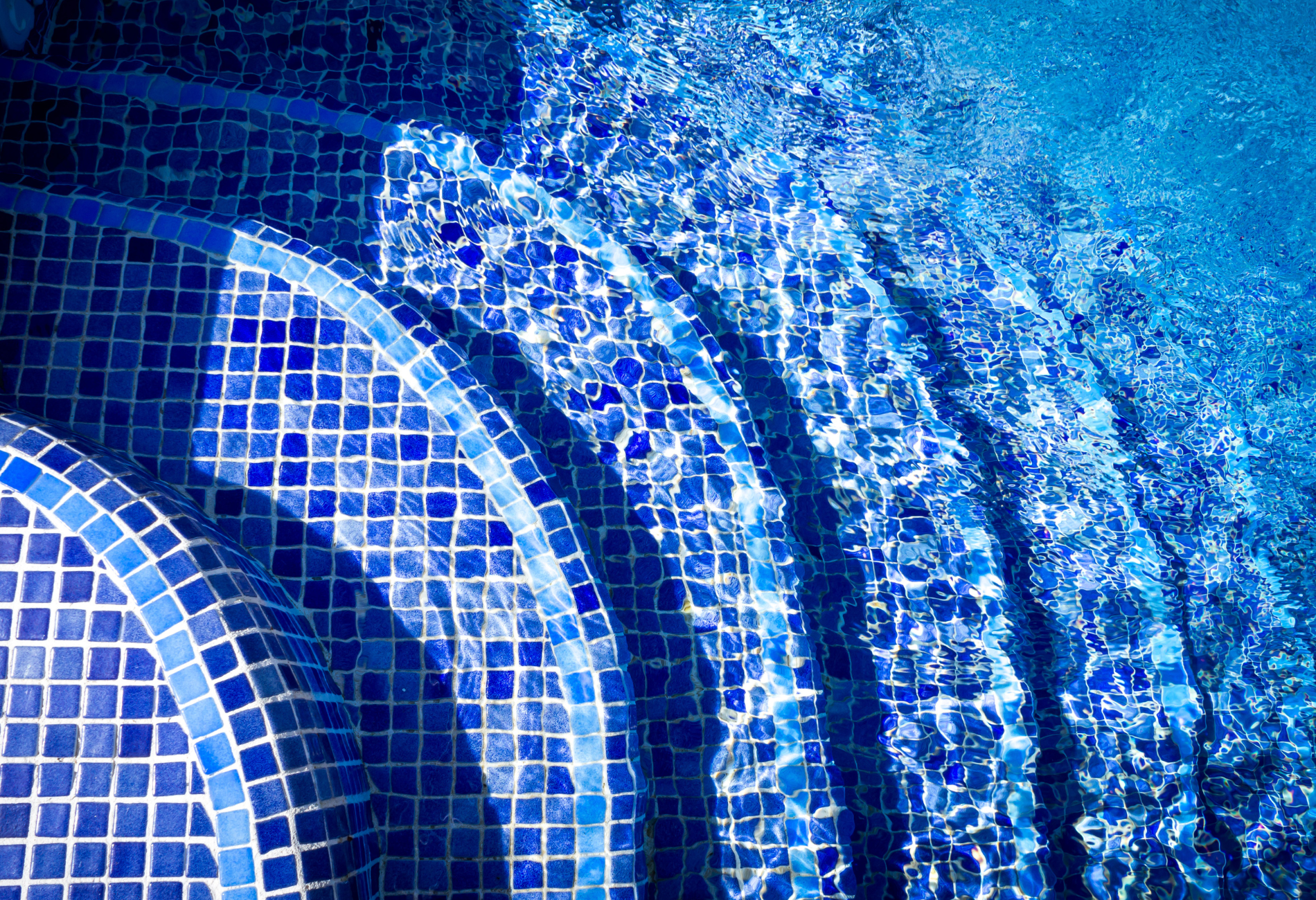 A close up of a swimming pool with blue tiles and stairs.
