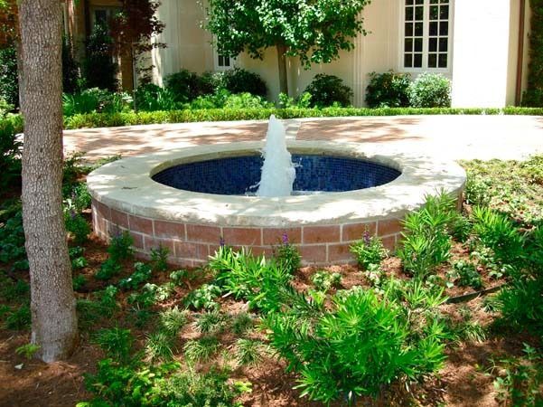 A fountain in the middle of a garden in front of a house