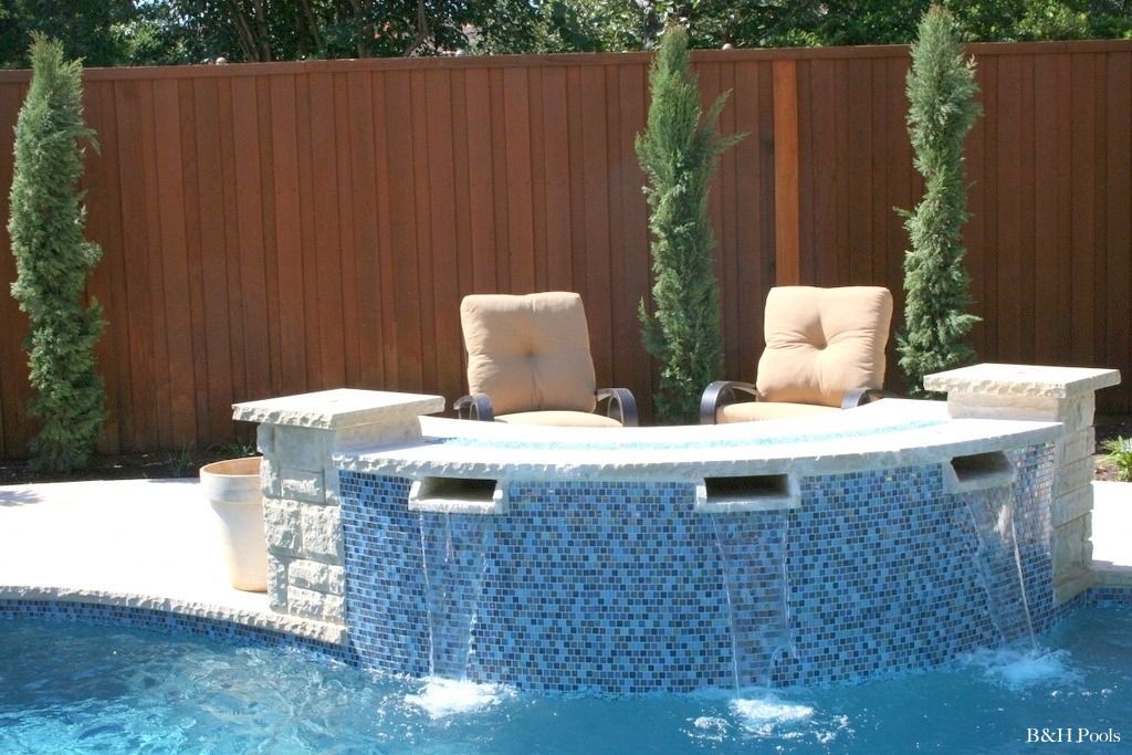 A wooden fence surrounds a swimming pool with a bar and chairs