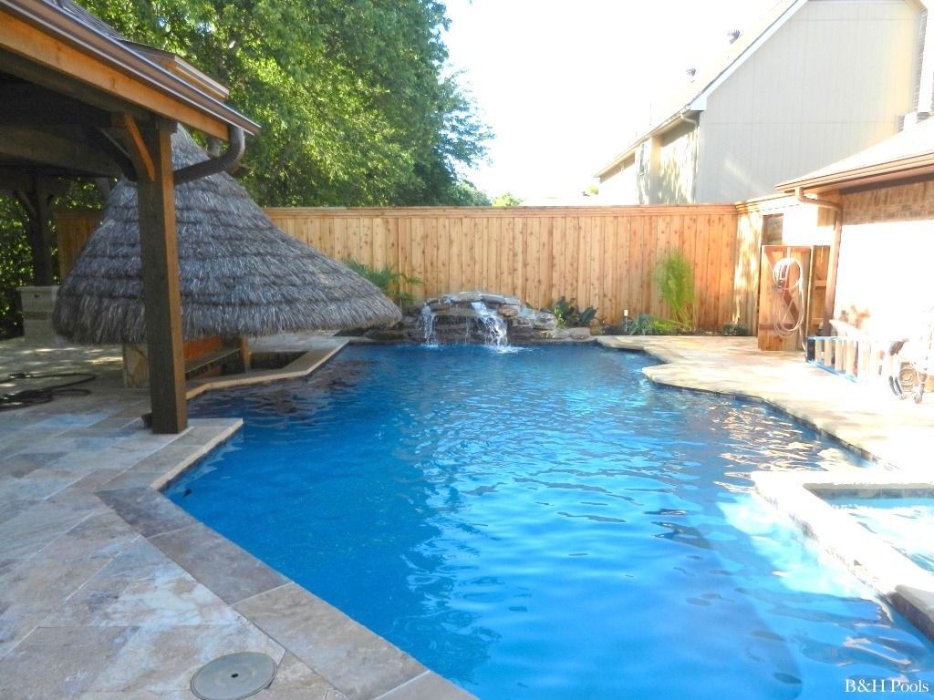 A large swimming pool with a thatched roof and a waterfall