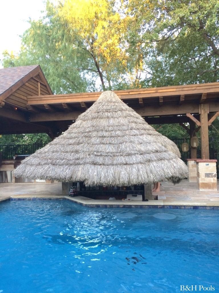 A large thatched roof over a swimming pool.
