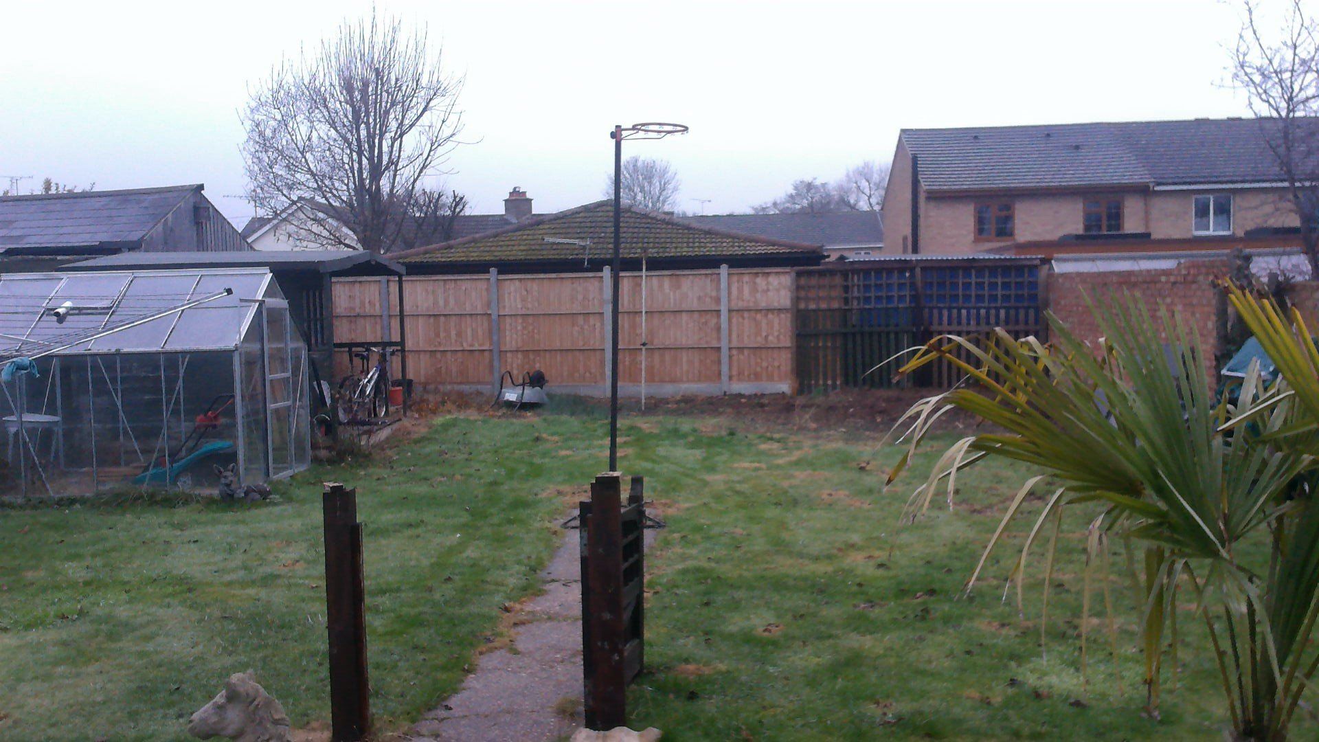 A backyard with a wooden fence and a greenhouse in the background.