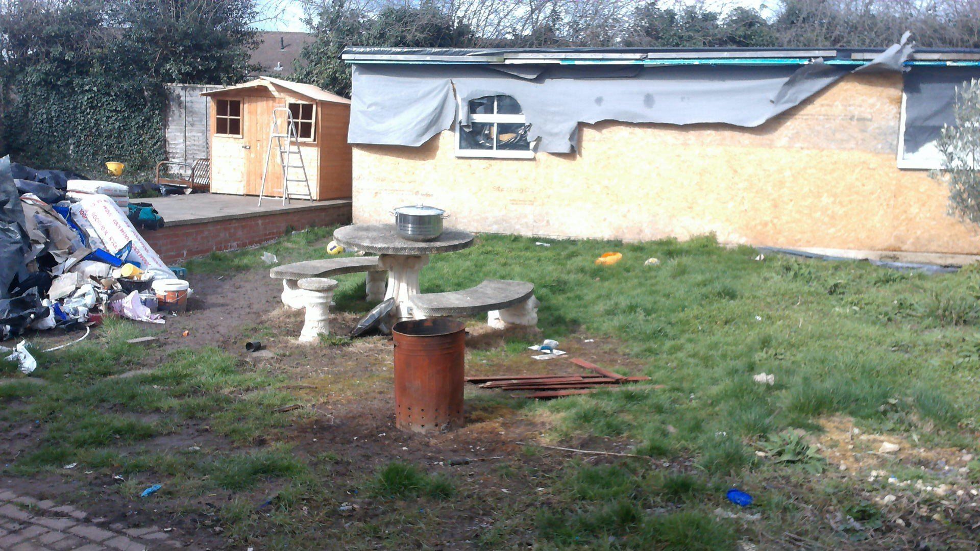 A shed with a tarp on the roof is sitting in the grass next to a picnic table