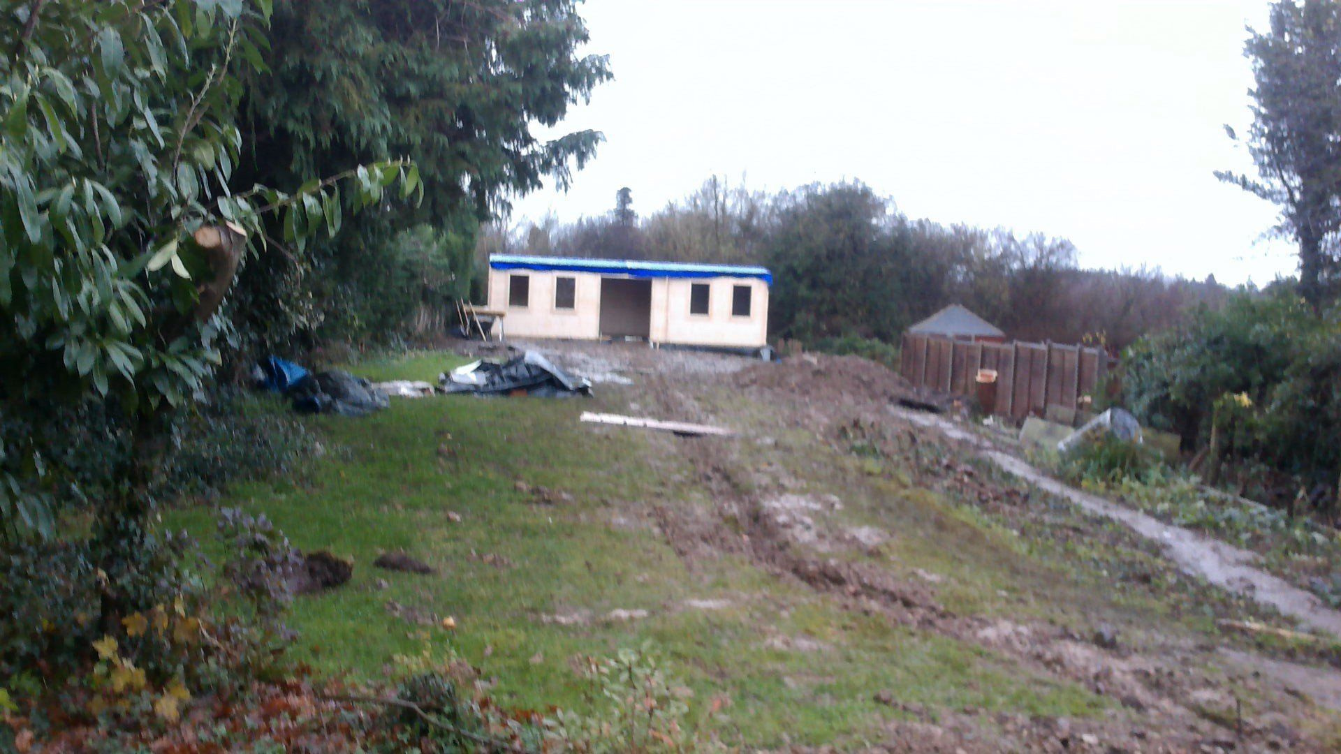 A small house is sitting on top of a dirt hill surrounded by trees.