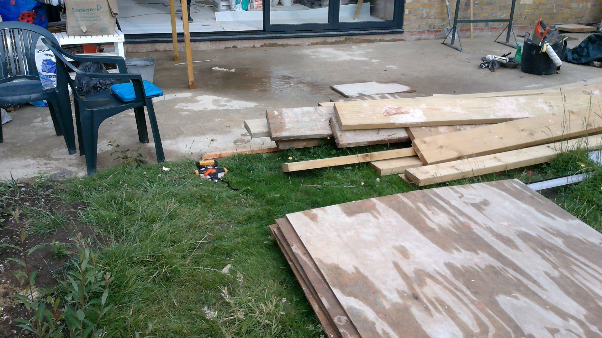 A pile of wood is sitting on the grass in a yard.