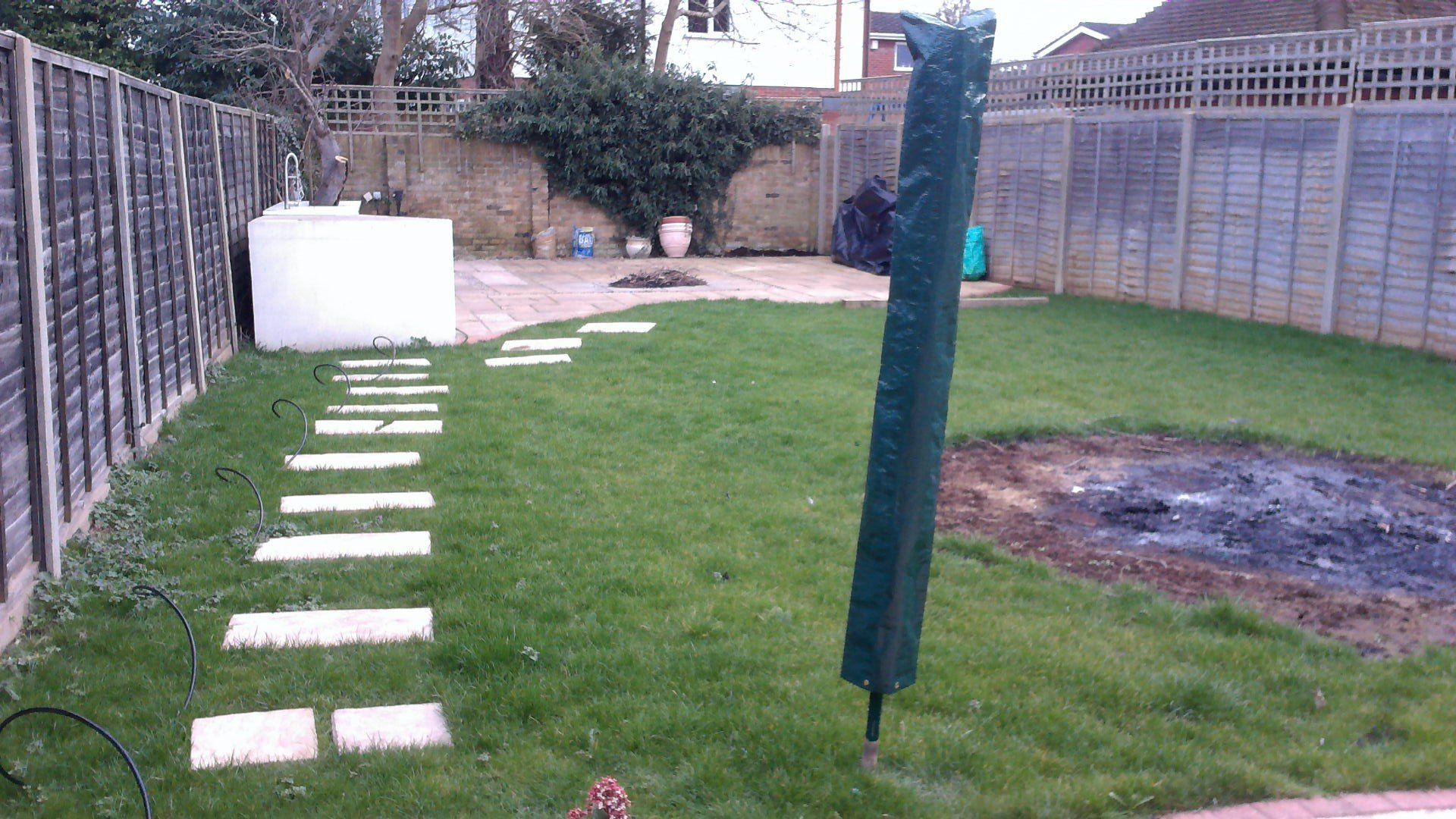 A backyard with a fence and a green umbrella.