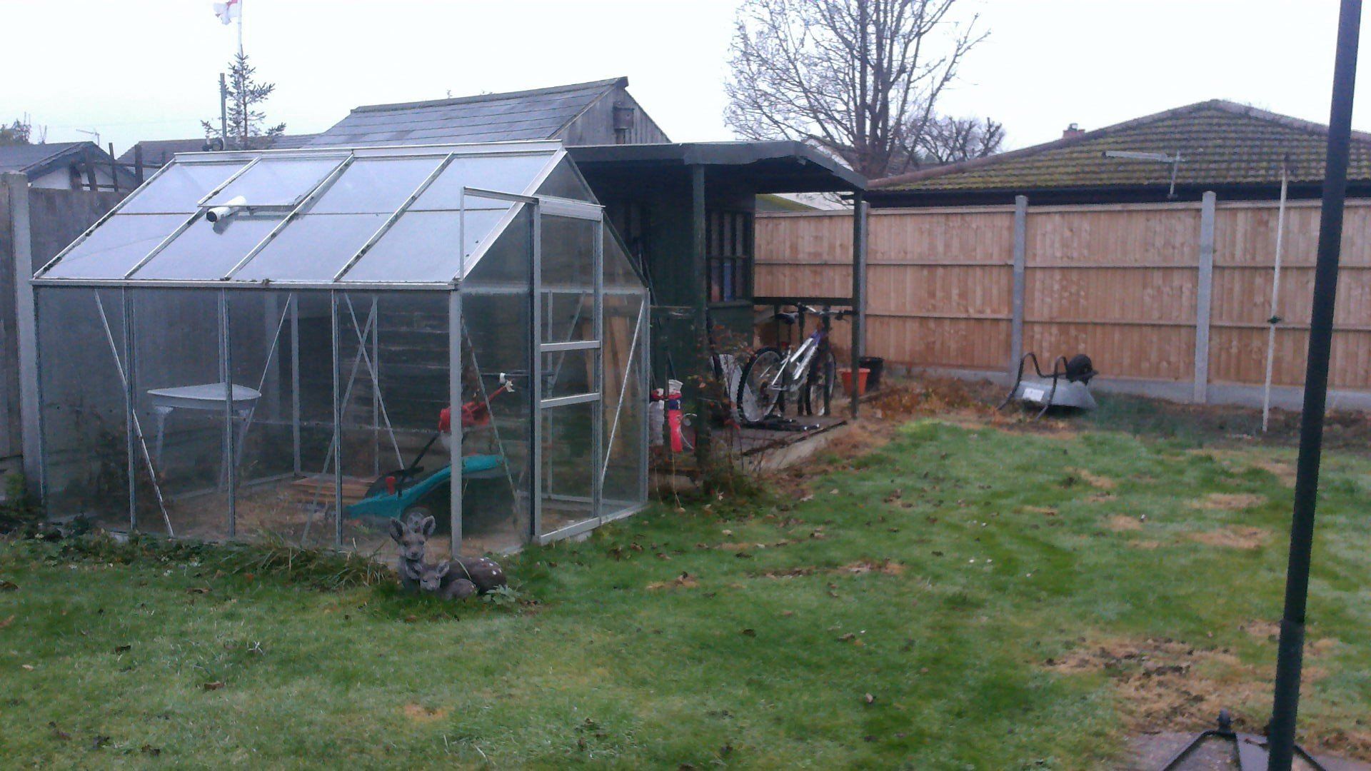 A greenhouse is sitting in the middle of a backyard next to a wooden fence.