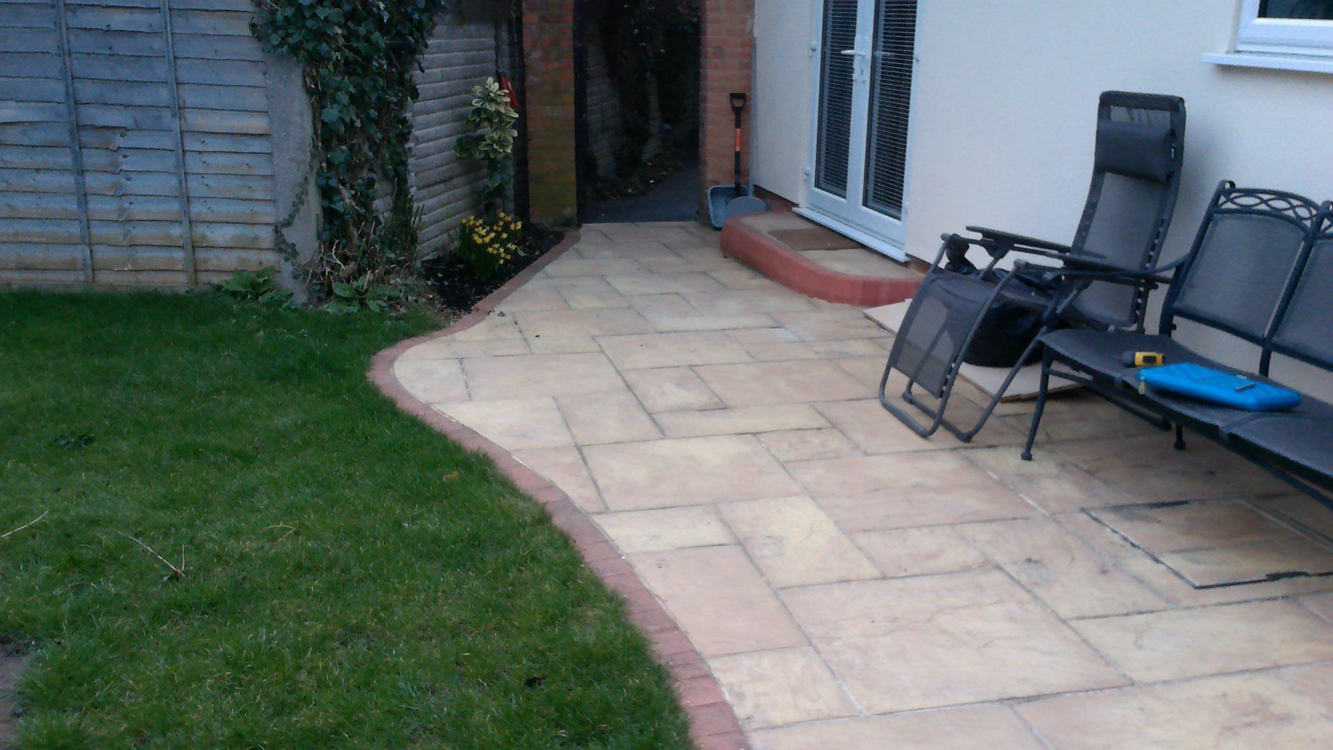 A patio with chairs and a bench in a backyard.