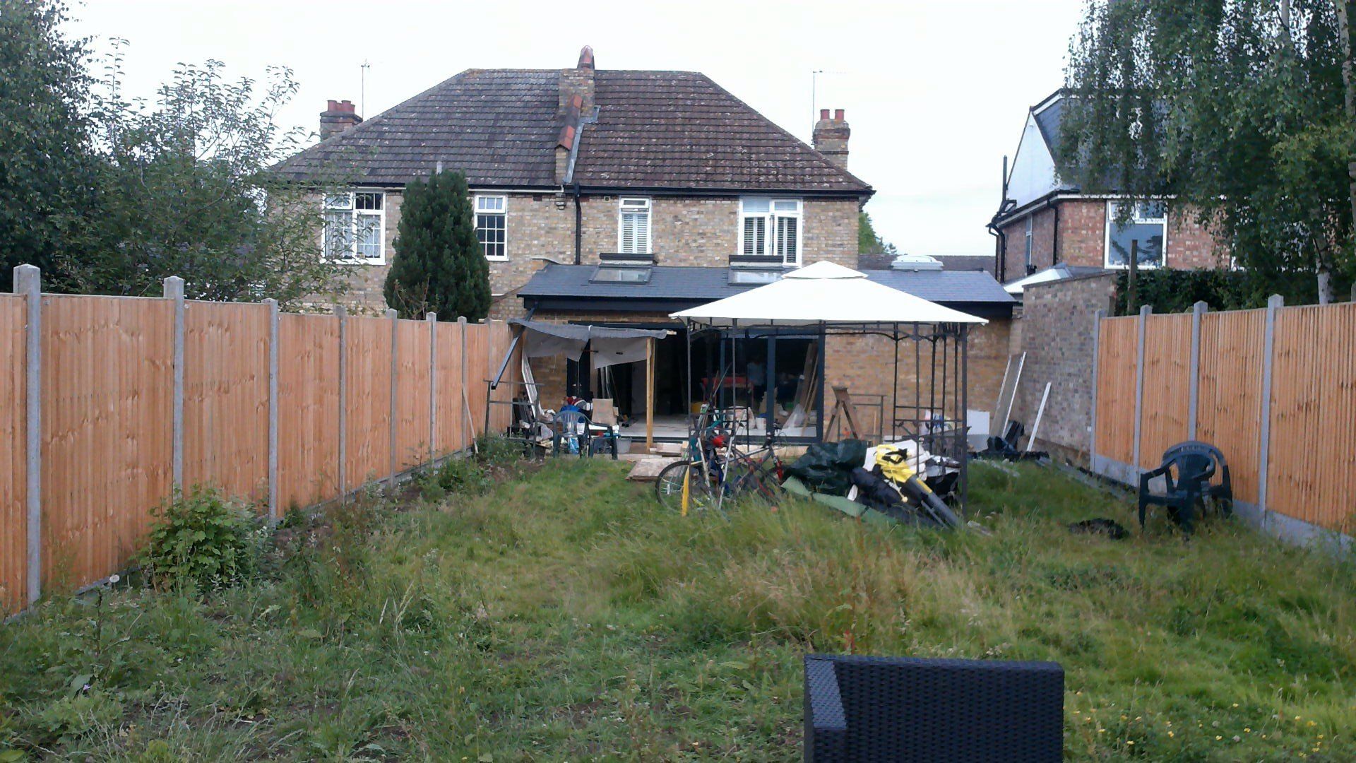 A backyard with a wooden fence and a house in the background