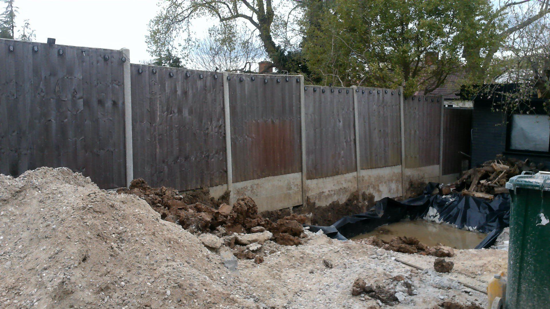 A pile of dirt is sitting in front of a wooden fence.