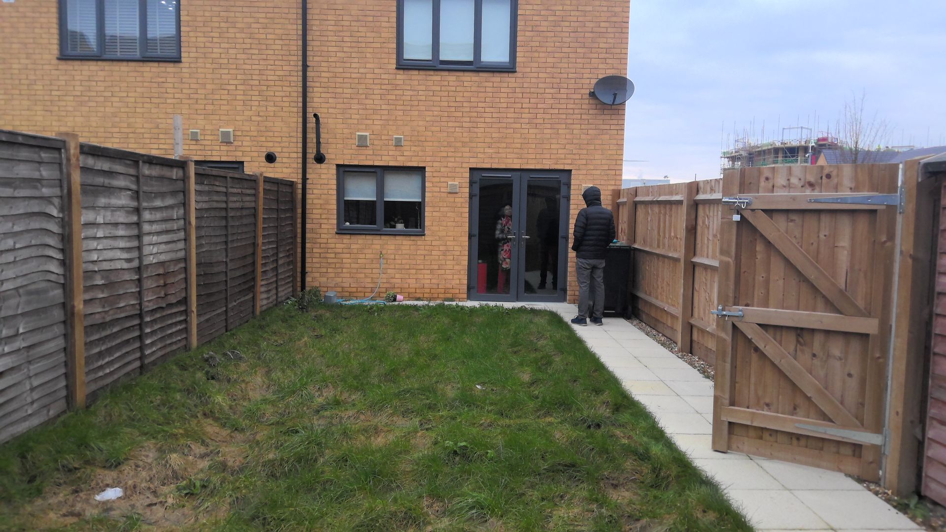 A man is standing in the backyard of a house next to a wooden fence.