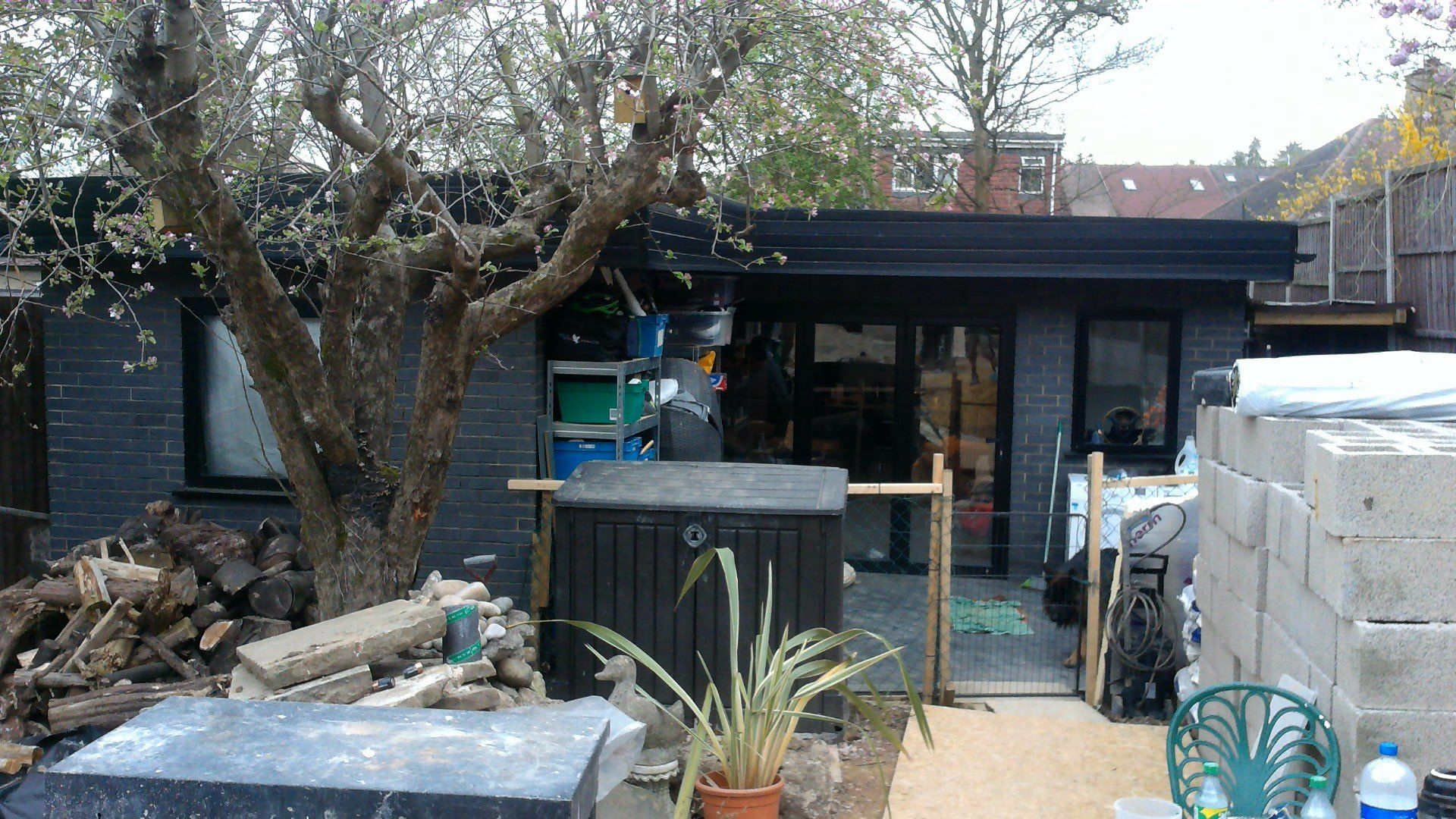 A black brick house with a tree in front of it.