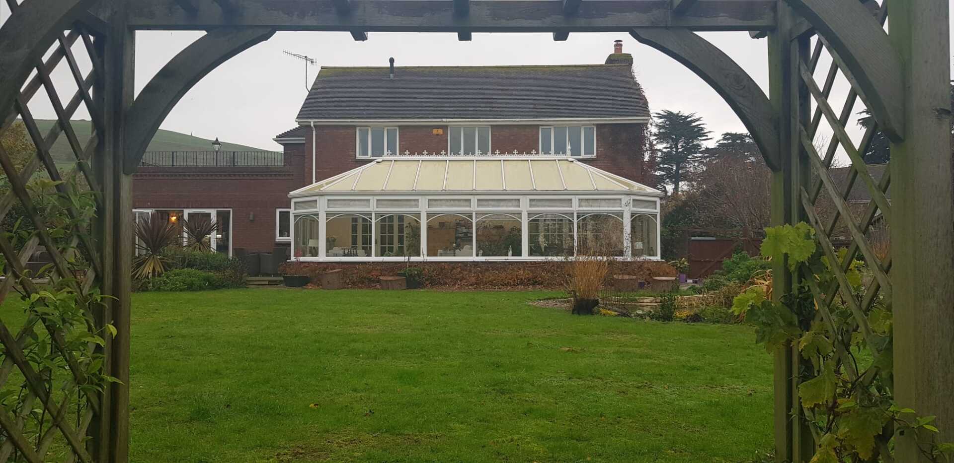 A large house with a greenhouse in the backyard is visible through a wooden archway.