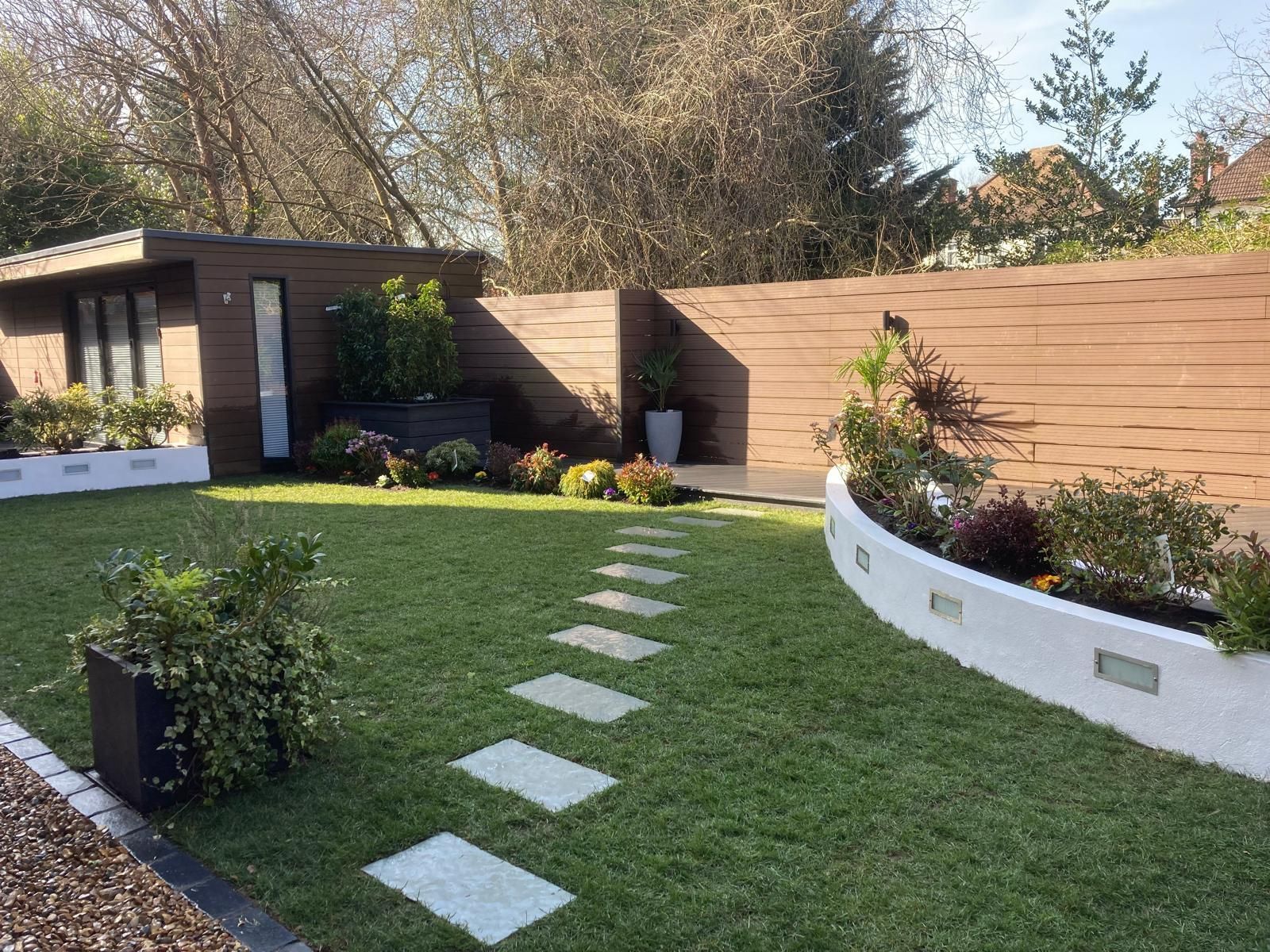 Well-manicured backyard with stepping stones leading to a garden shed. Green lawn, brown wooden fence, and flower beds create a tidy outdoor space.
