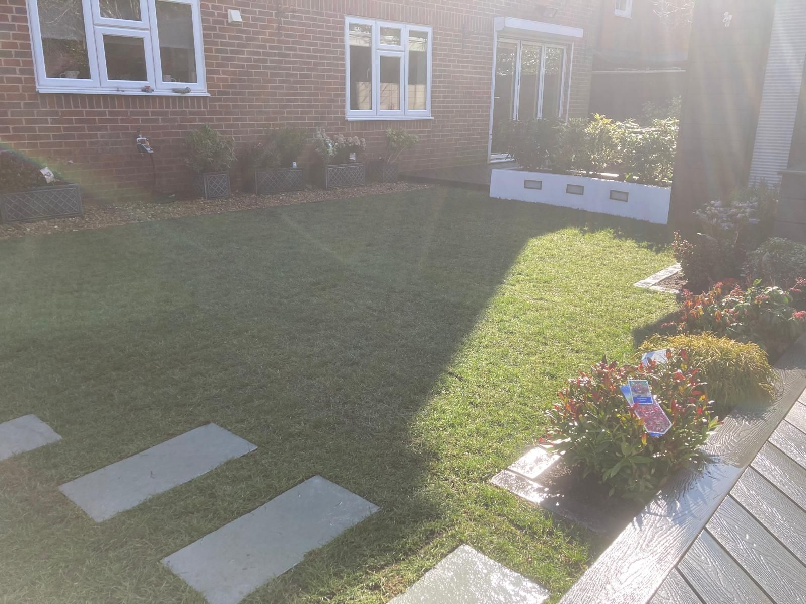 A well-kept front lawn with stepping stones leading to a brick house. Bright sunlight casts a shadow.