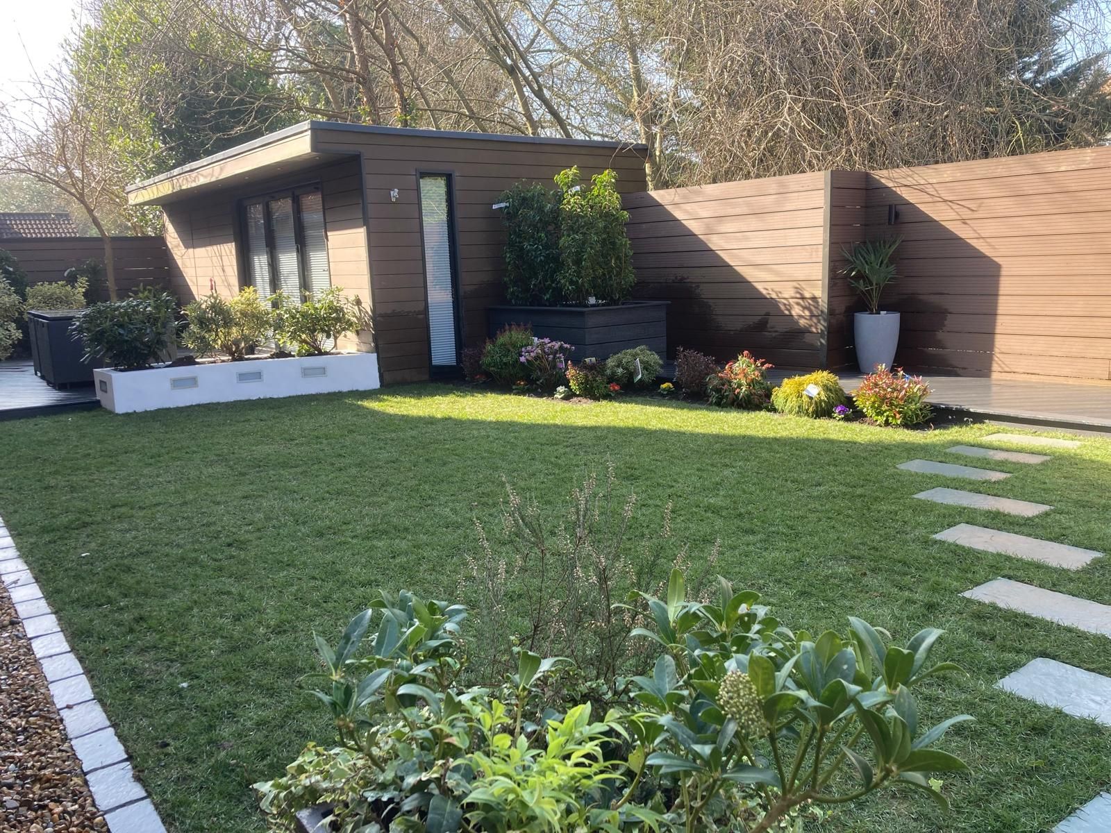A modern backyard with a shed, grass, and a stepping-stone path. Brown fencing and planters frame the space.