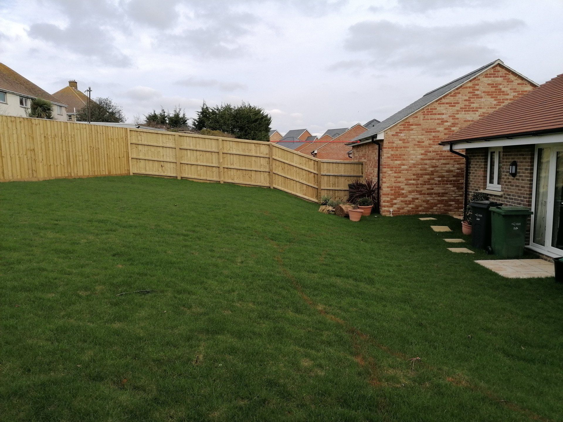 A backyard with a wooden fence and a house in the background