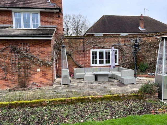 A patio with a couch , table and umbrella in front of a brick house.