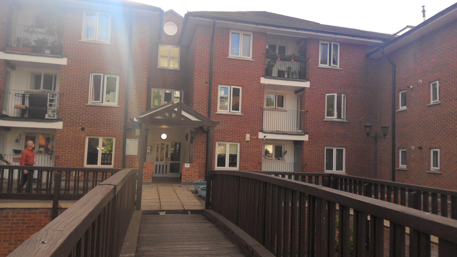 A wooden bridge leads to a brick apartment building