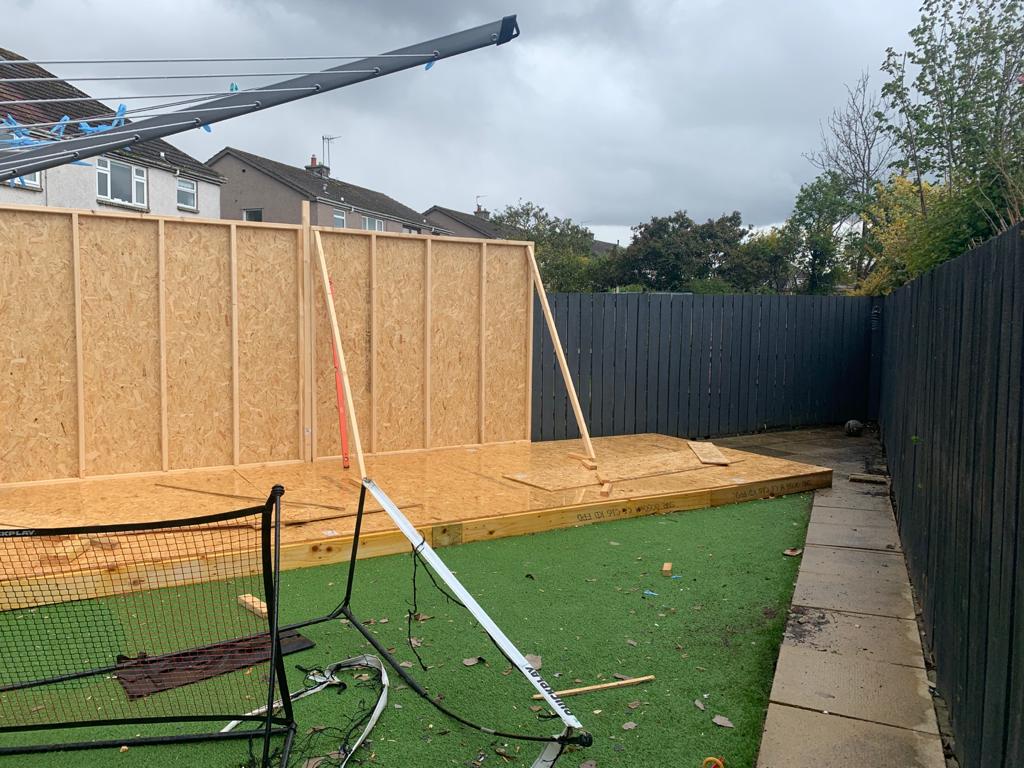 A backyard with a fence and a wooden wall being built.