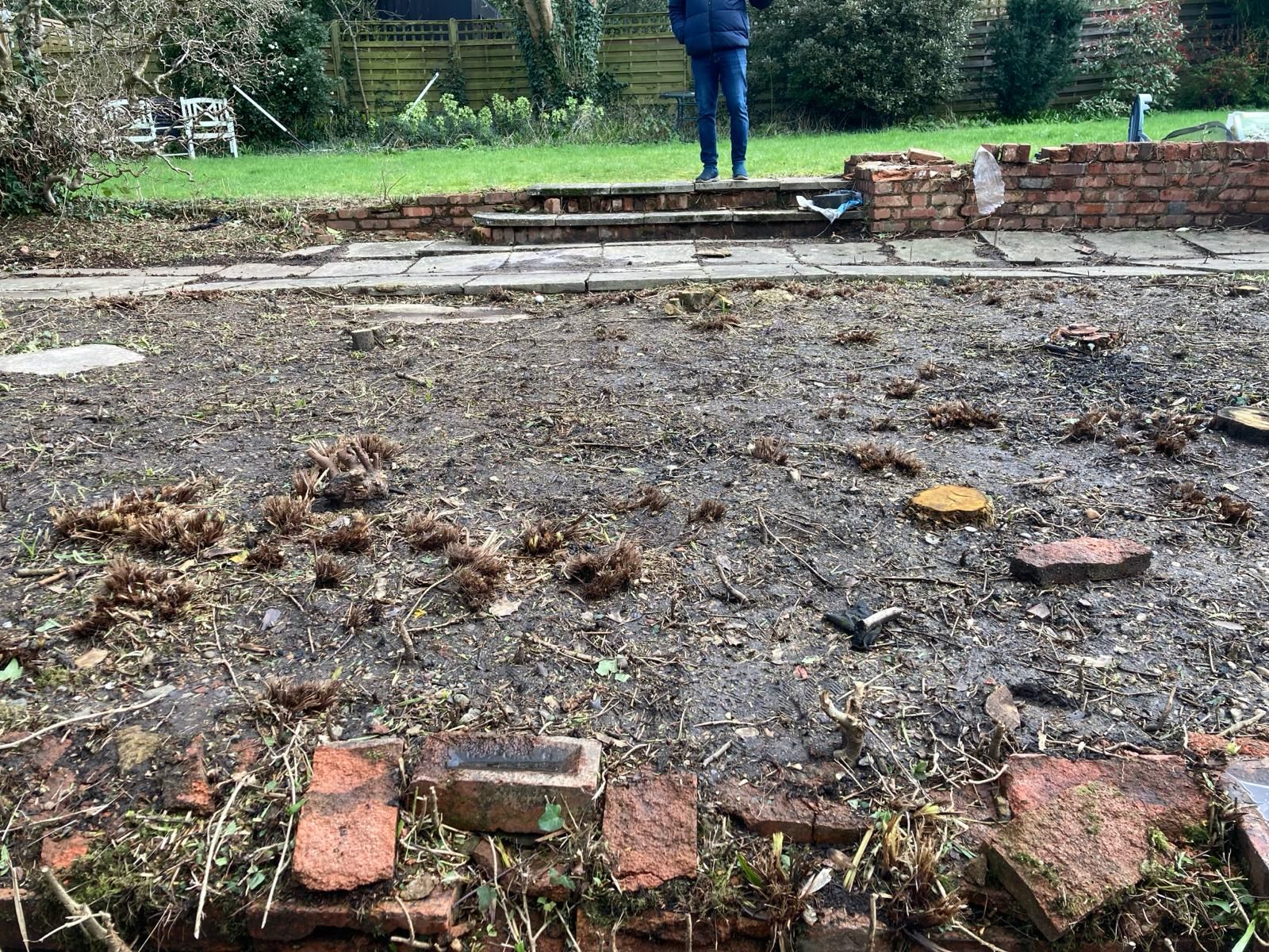 A man is standing in the middle of a dirt field next to a brick wall.