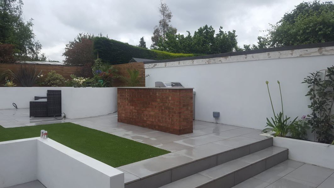 A patio with a grill and stairs in a backyard.