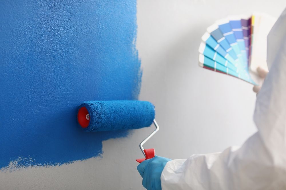 A person is painting a wall with a blue paint roller.