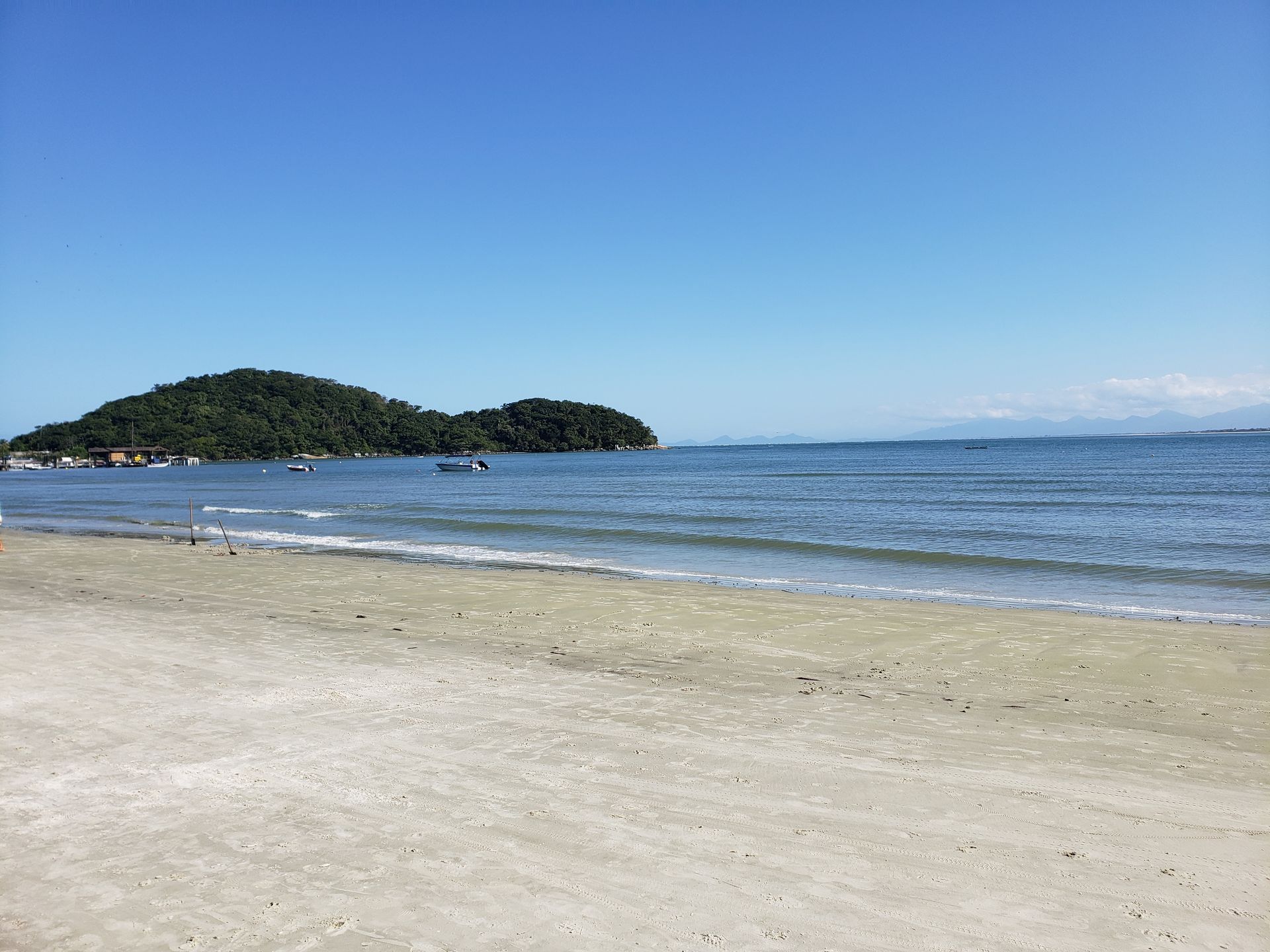 Uma praia com um barco na água e uma pequena ilha ao longe.