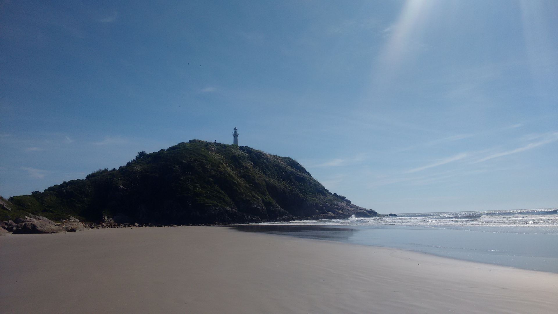 Uma praia com um farol no topo de uma colina ao longe.