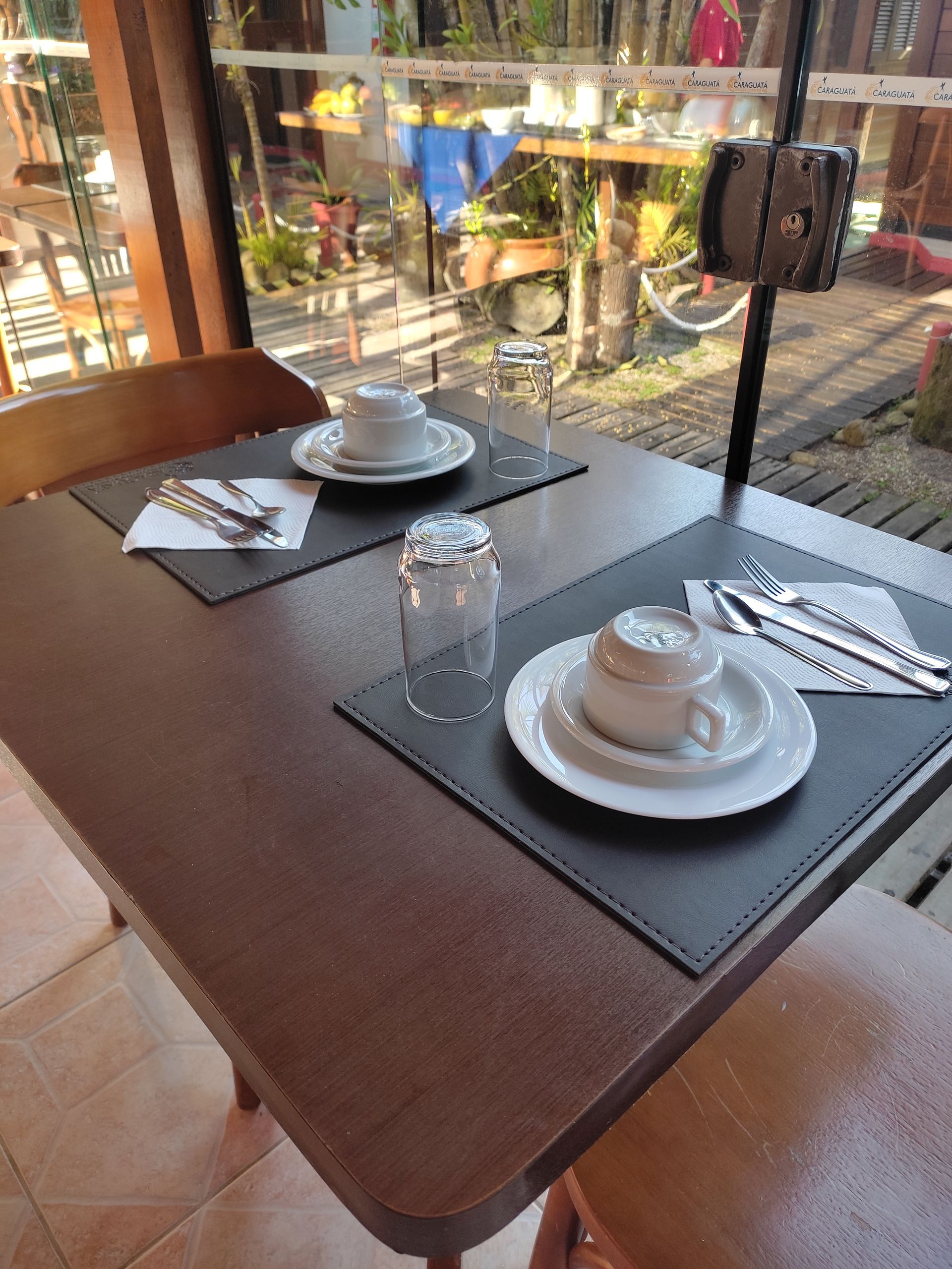 Uma mesa com pratos e copos em frente a uma janela.