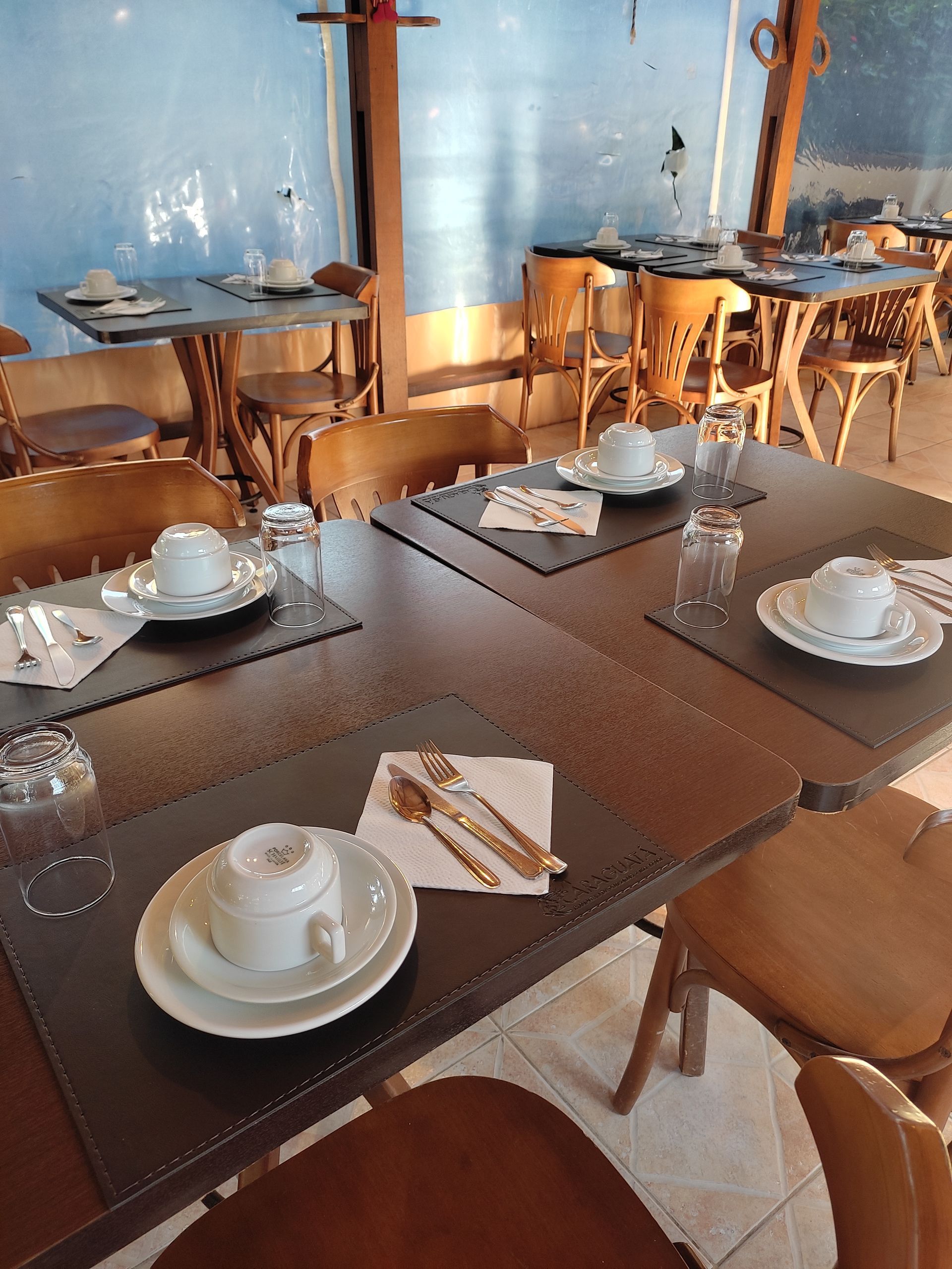 Um restaurante cheio de mesas e cadeiras com pratos e copos sobre elas.